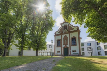 Rheinische Katholische Altenpflege, Kapelle im Innengelände mit Zuweg und Bäumen bei schönem Wetter, Außenansicht